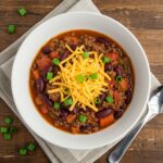 Chili végétarien copieux garni de cheddar râpé et d’oignons verts dans un bol blanc