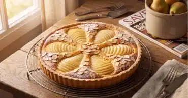Une magnifique tarte poires-amandes végétarienne fraîchement cuite, avec ses demi-poires tranchées en étoile sur un lit de crème d'amandes dorée, posée sur une grille de refroidissement ronde.